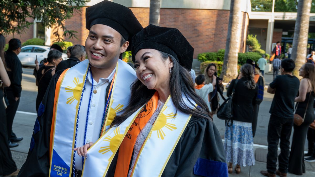 Two students in graduation attire smiling